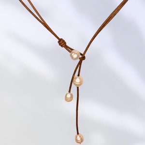 May include: A brown leather necklace with four off-white pearls hanging from it.