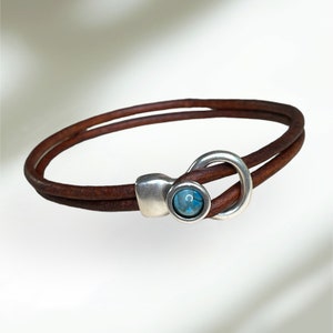 May include: A brown leather bracelet with a silver clasp featuring a blue gemstone.