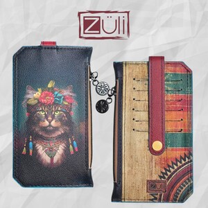 May include: A rectangular wallet with a black exterior featuring a cat wearing a floral crown and tassels, and a second wallet with a wood-grain pattern, horizontal stripes, and a red snap strap. Both items feature the Züli logo and metal charms.