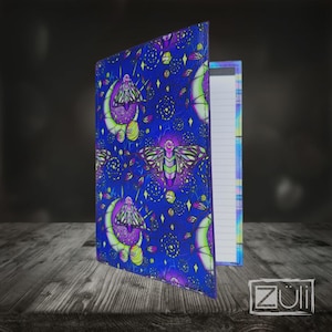 Peut inclure: Un carnet avec une couverture bleu vif ornée d'un motif répétitif de papillons de nuit, de croissants de lune et de petites étoiles dans des tons de violet, vert et jaune. Le carnet est entrouvert, révélant des pages lignées. Le logo Züli est visible.