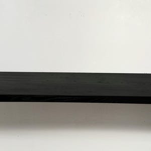 May include: A black wooden shelf with rounded edges. The shelf is made of solid wood and has a natural grain pattern.