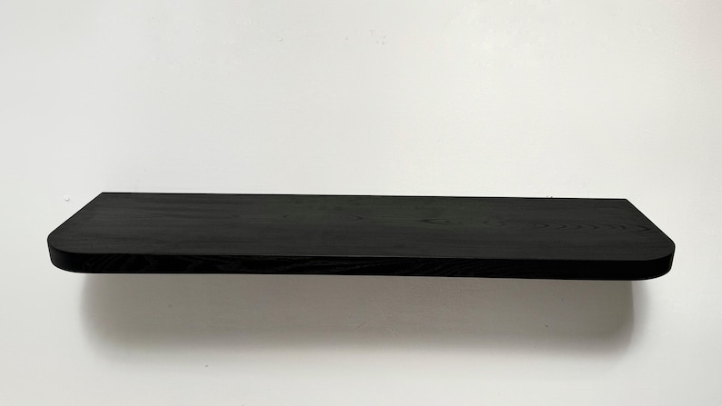 May include: A black wooden shelf with rounded edges. The shelf is made of solid wood and has a natural grain pattern.