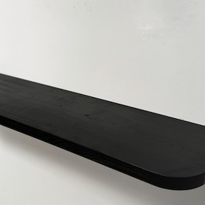 May include: A black wooden shelf with a rounded edge. The shelf is mounted to a white wall.