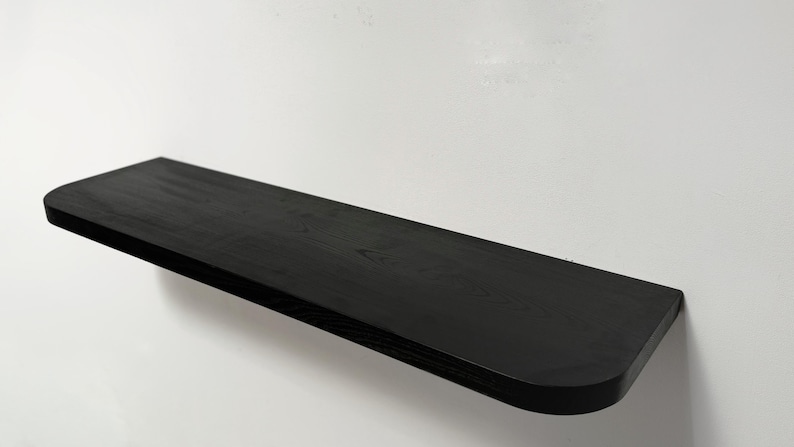 May include: A black wooden shelf with a rounded edge. The shelf is mounted to a white wall.