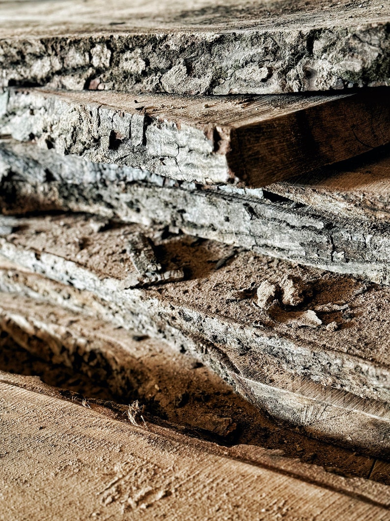 May include: A stack of rough-hewn wooden planks, showing the natural grain and texture of the wood. The planks are weathered and have a rustic appearance.
