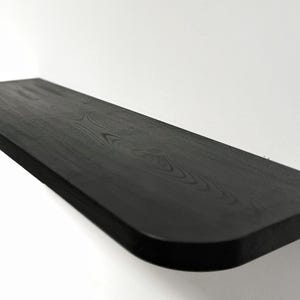 Könnte beinhalten: Ein schwarzes Holzregal mit abgerundeter Kante. Das Regal ist aus massivem Holz und hat eine natürliche Maserung.