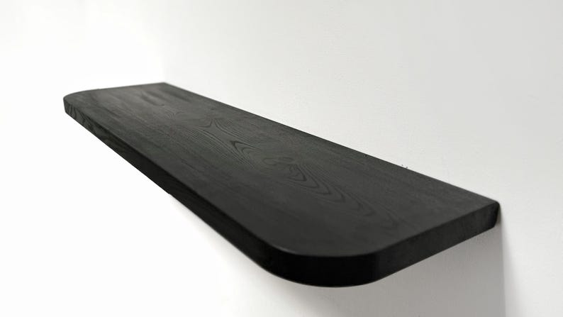 May include: A black wooden shelf with a rounded edge. The shelf is made of solid wood and has a natural grain pattern.