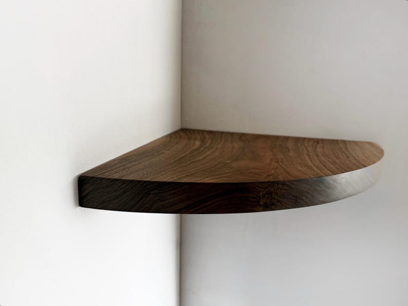 May include: A dark brown wooden corner shelf with a rounded edge. The shelf is mounted on a white wall.
