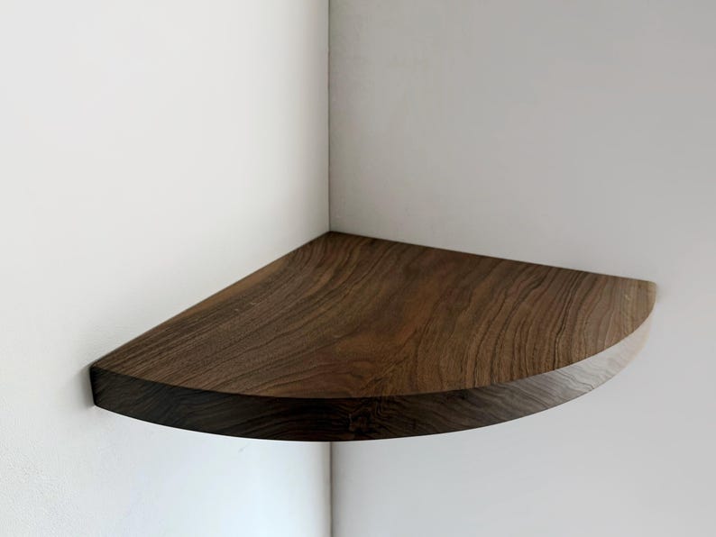 May include: A dark brown wooden corner shelf with a rounded edge. The shelf is mounted on a white wall.