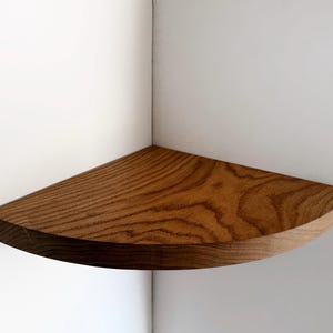 May include: A wooden corner shelf with a natural wood finish. The shelf is curved and has a rounded edge.