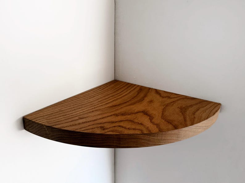 May include: A wooden corner shelf with a natural wood finish. The shelf is curved and has a rounded edge.
