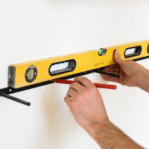 May include: A person uses a yellow level and a red pencil to mark a wall for a shelf installation.
