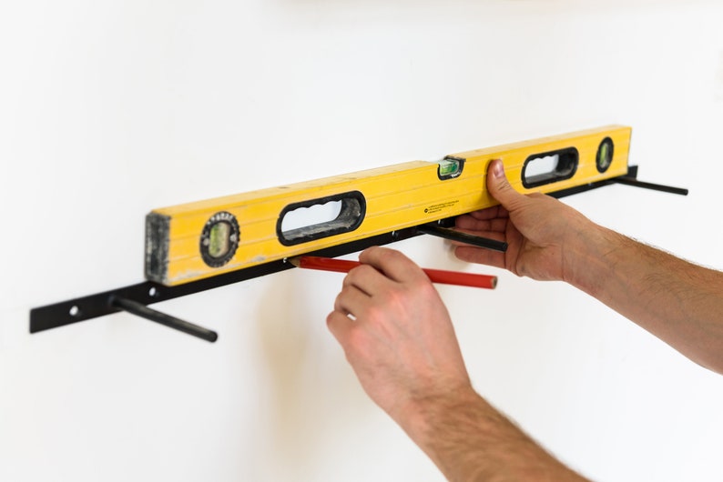 May include: A person uses a yellow level and a red pencil to mark a wall for a shelf installation.
