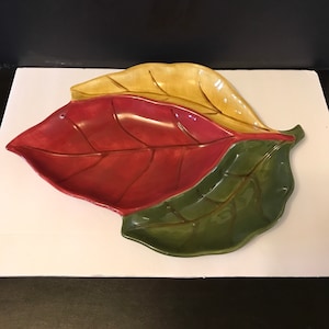 May include: A ceramic serving dish shaped like three overlapping leaves. The leaves are painted in shades of red, green, and yellow.