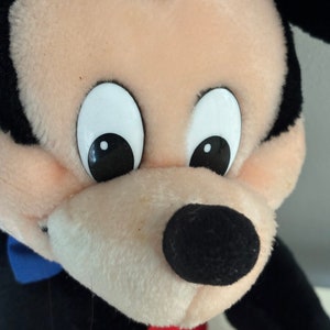 May include: A plush Mickey Mouse toy with black ears, a black nose, and white eyes. The toy is wearing a red and black outfit.