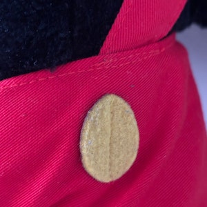 May include: Close-up of a red fabric with a brown button. The button is oval-shaped and has a textured surface.