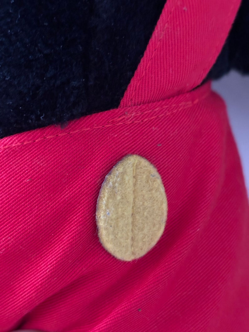 May include: Close-up of a red fabric with a brown button. The button is oval-shaped and has a textured surface.