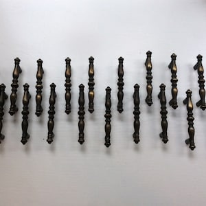 May include: A collection of 20 antique-style cabinet knobs with a dark bronze finish. The knobs have a simple, elegant design with a rounded top and a fluted body.