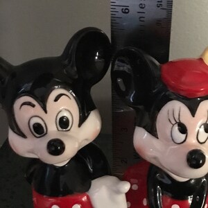 Pu&ograve; includere: Una statuetta in ceramica bianca e nera di Topolino che indossa pantaloncini rossi con pois bianchi. Accanto a lui c'&egrave; una statuetta in ceramica bianca e nera di Topolina che indossa un vestito rosso con pois bianchi e un fiocco rosso.