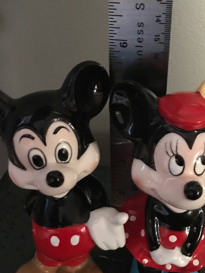 Pu&ograve; includere: Una statuetta in ceramica bianca e nera di Topolino che indossa pantaloncini rossi con pois bianchi. Accanto a lui c'&egrave; una statuetta in ceramica bianca e nera di Topolina che indossa un vestito rosso con pois bianchi e un fiocco rosso.