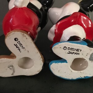 Pu&ograve; includere: Un paio di figurine in ceramica di Topolino e Minnie Mouse. Entrambe le figurine indossano abiti rossi e bianchi. La parte inferiore di ogni figurina ha una base blu e bianca con il testo "DISNEY JAPAN" stampato sul fondo.