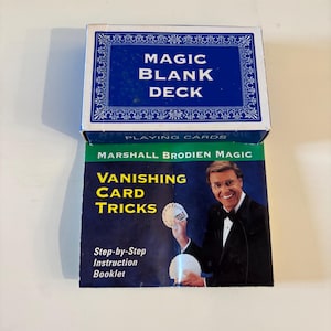 May include: A blue and white "MAGIC BLANK DECK" playing card box sits atop a booklet titled "VANISHING CARD TRICKS" by Marshall Brodien. The booklet features a photo of a smiling man in a tuxedo holding playing cards. The booklet also includes "Step-by-Step Instruction Booklet".