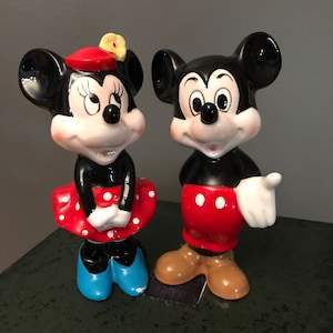 Pu&ograve; includere: Un set di figurine in ceramica vintage di Topolino e Minnie Mouse. Topolino indossa pantaloncini rossi con pois bianchi e scarpe marroni. Minnie indossa un vestito rosso con pois bianchi, un cappello rosso con un fiore giallo e scarpe blu.