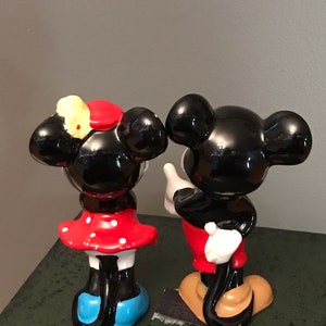 Pu&ograve; includere: Un set di figurine in ceramica di Topolino e Minnie Mouse. Topolino indossa pantaloncini rossi e scarpe nere. Minnie indossa un vestito a pois rossi e bianchi e scarpe blu. Entrambe le figurine hanno orecchie nere e occhi neri.