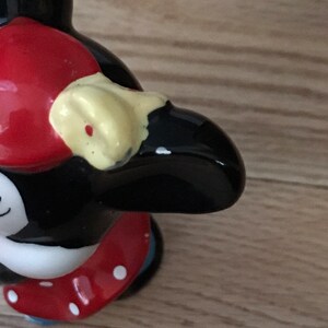 Pu&ograve; includere: Una statuetta di ceramica nera e bianca di un pinguino che indossa un cappello rosso con pois bianchi e un becco giallo. Il pinguino indossa una gonna rossa con pois bianchi e pantaloni blu.