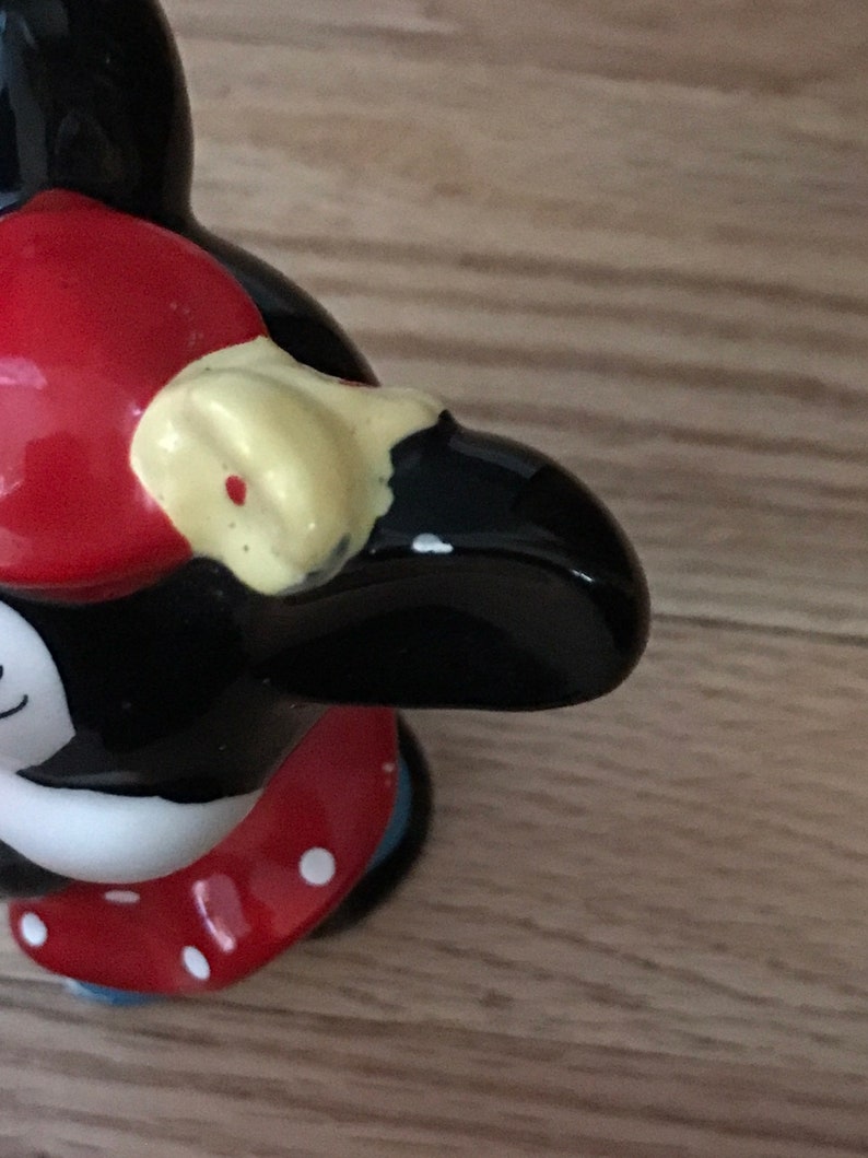 Pu&ograve; includere: Una statuetta di ceramica nera e bianca di un pinguino che indossa un cappello rosso con pois bianchi e un becco giallo. Il pinguino indossa una gonna rossa con pois bianchi e pantaloni blu.