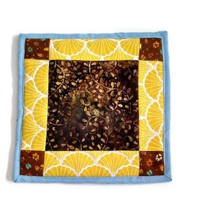 Può includere: Un quadrato di trapunta patchwork blu e giallo con un motivo floreale marrone al centro. Il quadrato è fatto di diversi tessuti con una varietà di motivi.