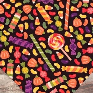 May include: A black bandana with a Halloween candy pattern. The pattern includes candy corn, lollipops, jelly beans, and wrapped candies in various colors.