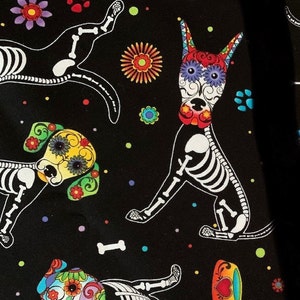 May include: Black fabric with a repeating pattern of colorful sugar skull dogs. The dogs are skeletons with floral designs and bright colors. The background is black with white bones and colorful dots.