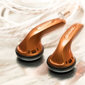 May include: A pair of copper-colored in-ear headphones with black earpieces. The headphones have the text "VE MONK" printed on the side.