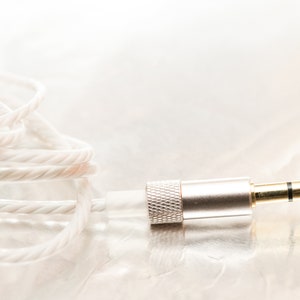 K&ouml;nnte beinhalten: Nahaufnahme eines wei&szlig;en geflochtenen Audiokabels mit einem vergoldeten 3,5-mm-Klinkenstecker.