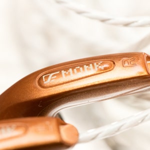 K&ouml;nnte beinhalten: Nahaufnahme eines Paares kupferfarbener In-Ear-Kopfh&ouml;rer mit dem Markennamen "FiiO" und dem Buchstaben "R" auf der Seite.