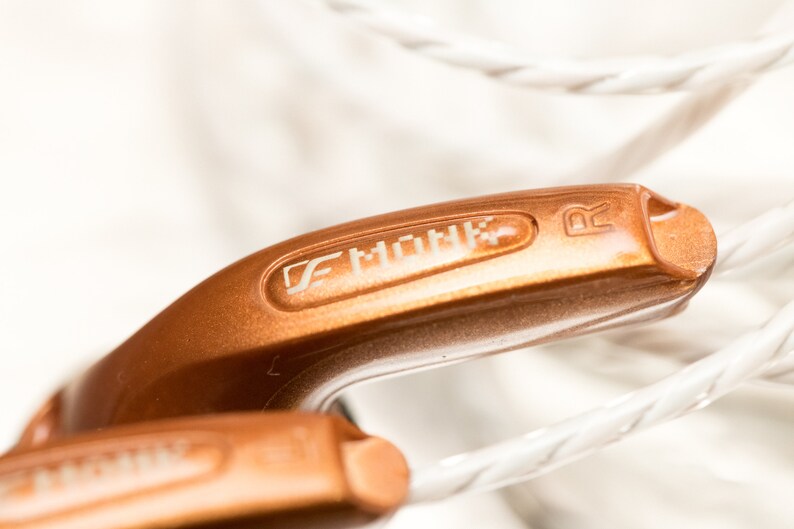 K&ouml;nnte beinhalten: Nahaufnahme eines Paares kupferfarbener In-Ear-Kopfh&ouml;rer mit dem Markennamen "FiiO" und dem Buchstaben "R" auf der Seite.