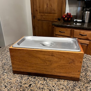 May include: A wooden box with a stainless steel insert. The box is made of light brown wood with a darker brown wood trim. The insert has a handle on the top.