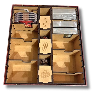 May include: A wooden organizer with compartments for storing game pieces and cards. The organizer has a brown and red patterned exterior and features a claw mark design on one of the compartments.