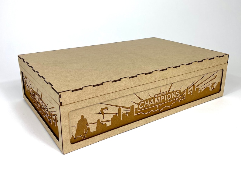 May include: A brown cardboard box with a cutout design of a city skyline and the words "MARVEL CHAMPIONS" on the front.