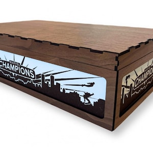 May include: A wooden box with a light blue interior and a black silhouette of a city skyline with the text "MARVEL CHAMPIONS" on a sign. The box is closed.