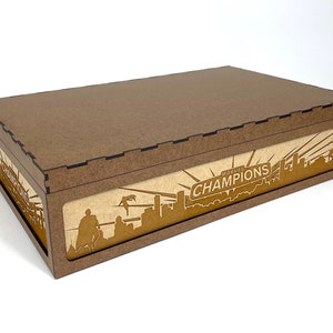 May include: A brown wooden box with a lid. The box has a Marvel Champions logo on the front with a cityscape and a superhero silhouette.