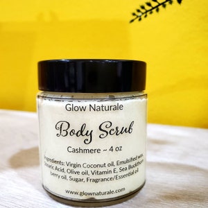May include: A clear glass jar with a black lid, labeled "Glow Naturale Body Scrub Cashmere." The jar contains a white, granular substance and is approximately 4 oz. Ingredients listed include coconut oil, olive oil, and vitamin E. The website www.glownaturale.com is also visible.