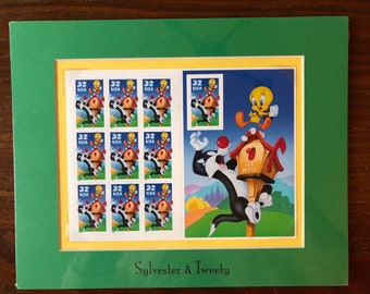 May include: A framed print featuring a collection of 12 Sylvester and Tweety Bird postage stamps. The stamps are arranged in a grid of four rows and three columns. The stamps feature Sylvester the cat chasing Tweety Bird. The print also includes a larger image of Sylvester and Tweety Bird in a scene with a mailbox. The print is titled "Sylvester & Tweety".