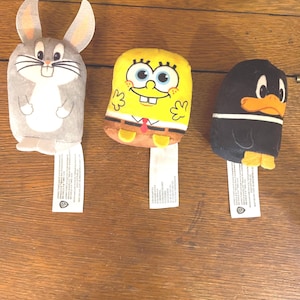 May include: Three plush toys: Bugs Bunny, SpongeBob SquarePants, and Daffy Duck. The toys are all in a sitting position and have a white tag attached to their feet.