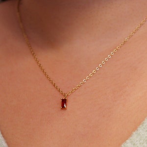 May include: A gold chain necklace with a small, rectangular red gemstone pendant.