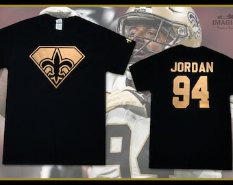 May include: Two black t-shirts with gold designs. The front shirt has a gold fleur-de-lis in a diamond shape. The back shirt has the name "JORDAN" and the number "94" in gold.
