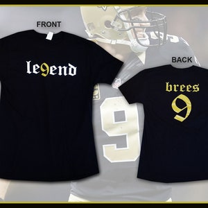 May include: Black t-shirts with gold and white text. The front shirt says "legend" in a gothic font. The back shirt says "brees 9" in a similar font. The shirts are likely sports-themed apparel.