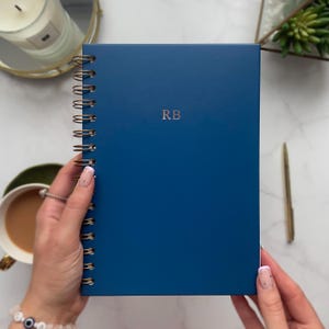 May include: A blue spiral bound notebook with the initials "RB" embossed in gold on the front cover.