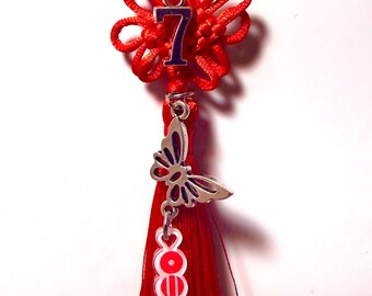 May include: A red decorative charm with a white pearl bead, a red flower knot, and a silver butterfly charm. The charm features the number 7 in blue and a red tassel with a white and red design.